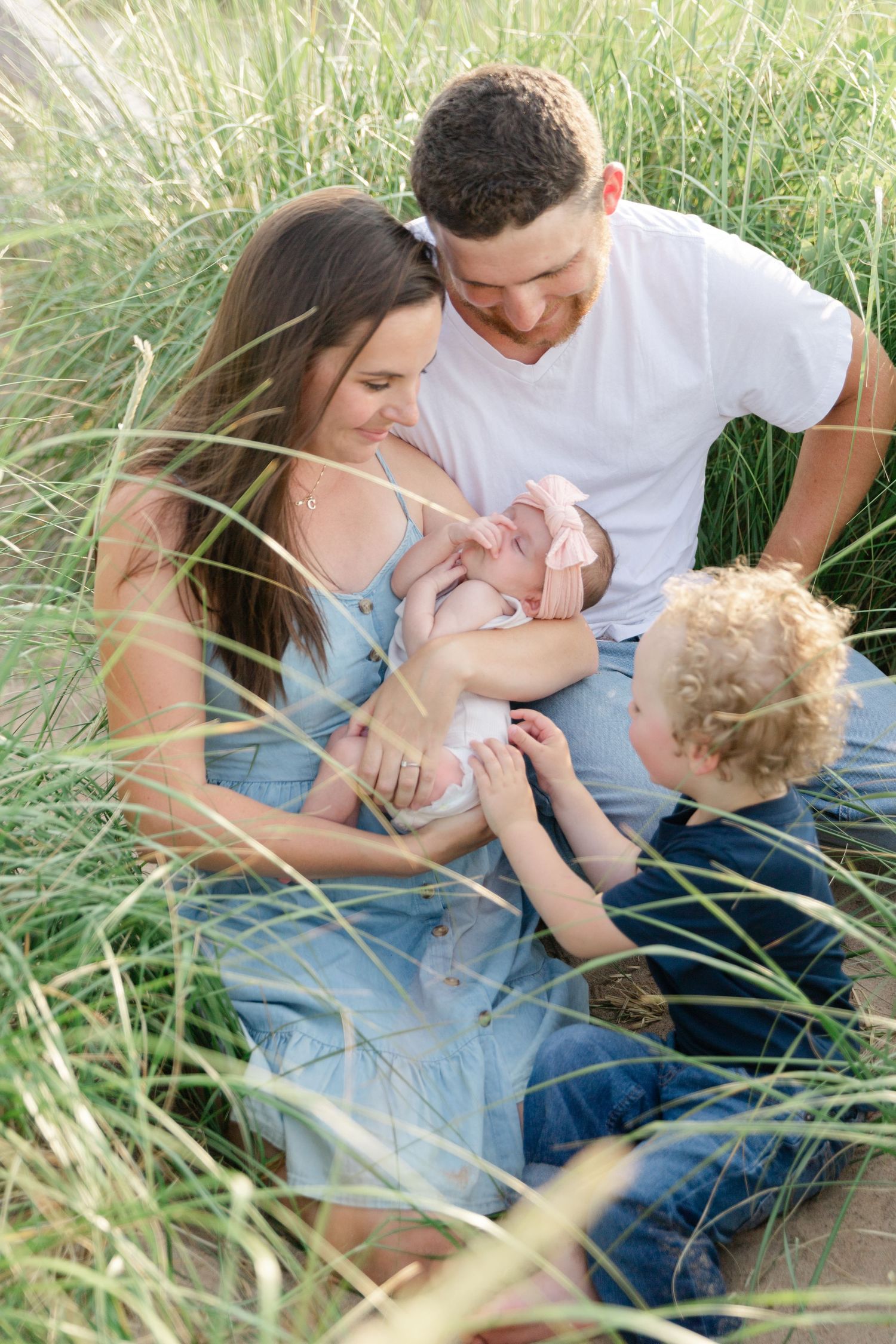 A family sits together in tall summer grass while sharing an intimate moment on a sunny afternoon.