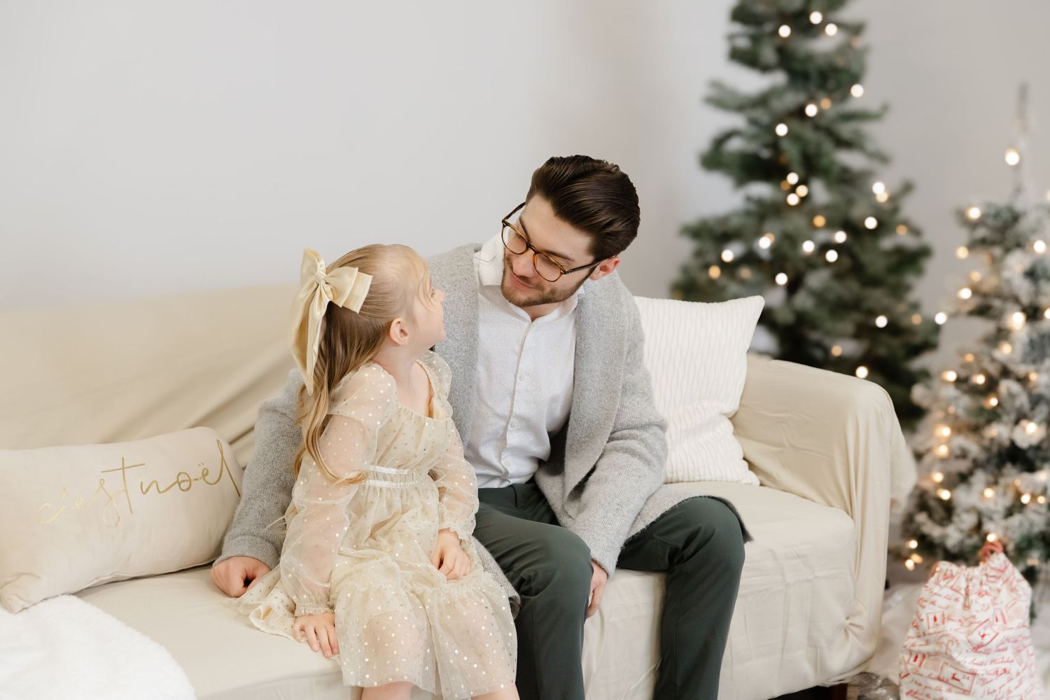 Two people sit on a beige couch having a heartwarming conversation during Christmas, with a decorated tree in background.