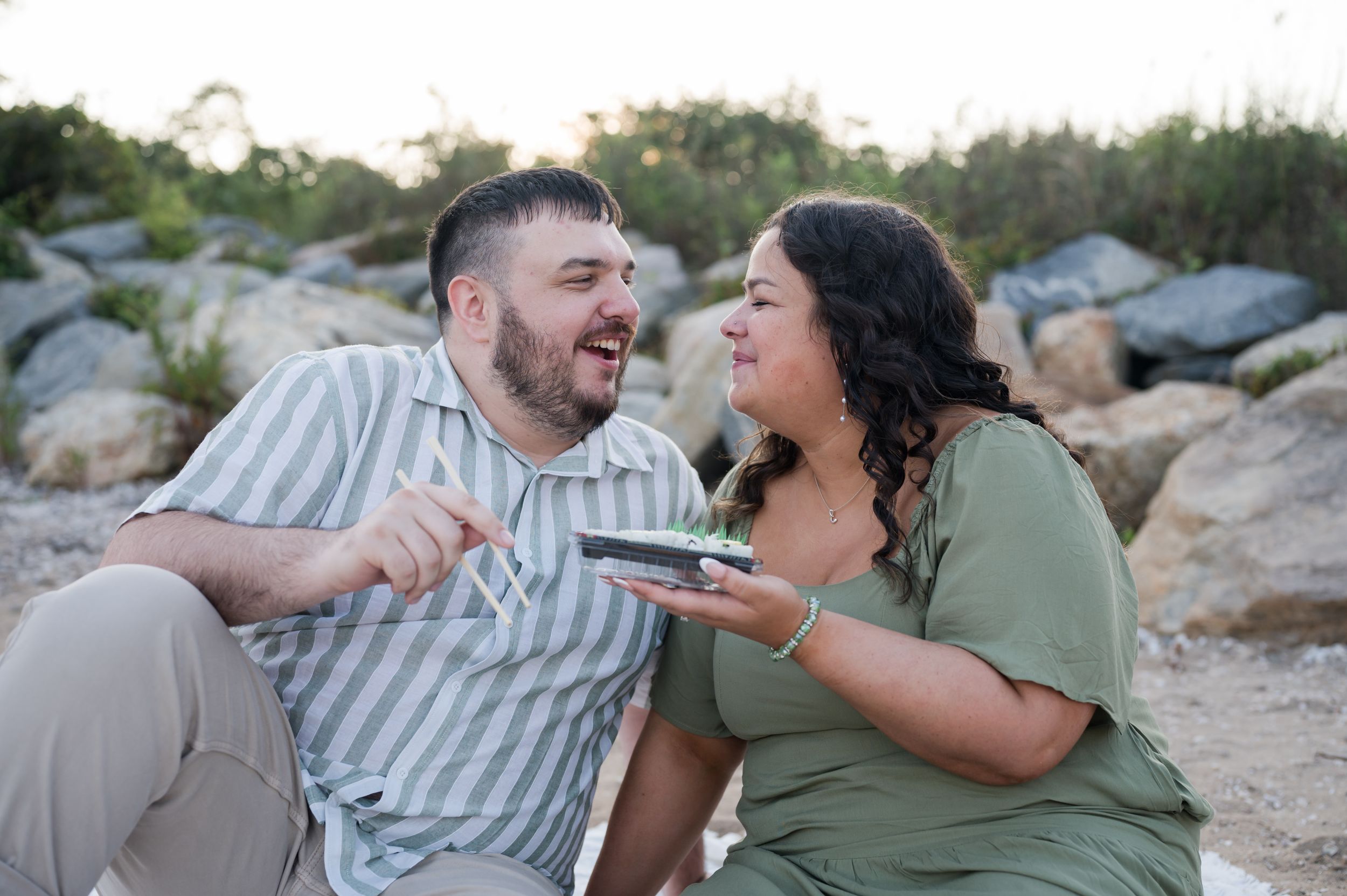 A couple shares a joyful moment while lying on rocky terrain at sunset. Hammonasset Beach State Park