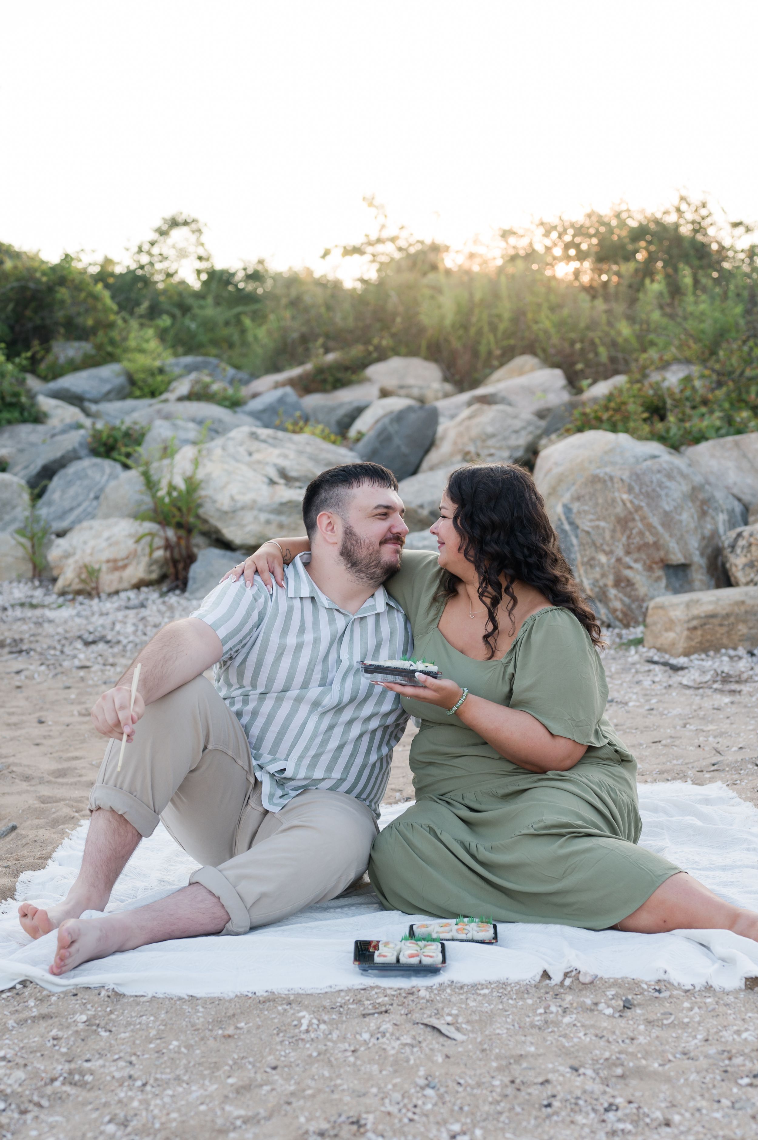 Two people relax on a blanket among coastal rocks during golden hour. Hammonasset Beach State Park