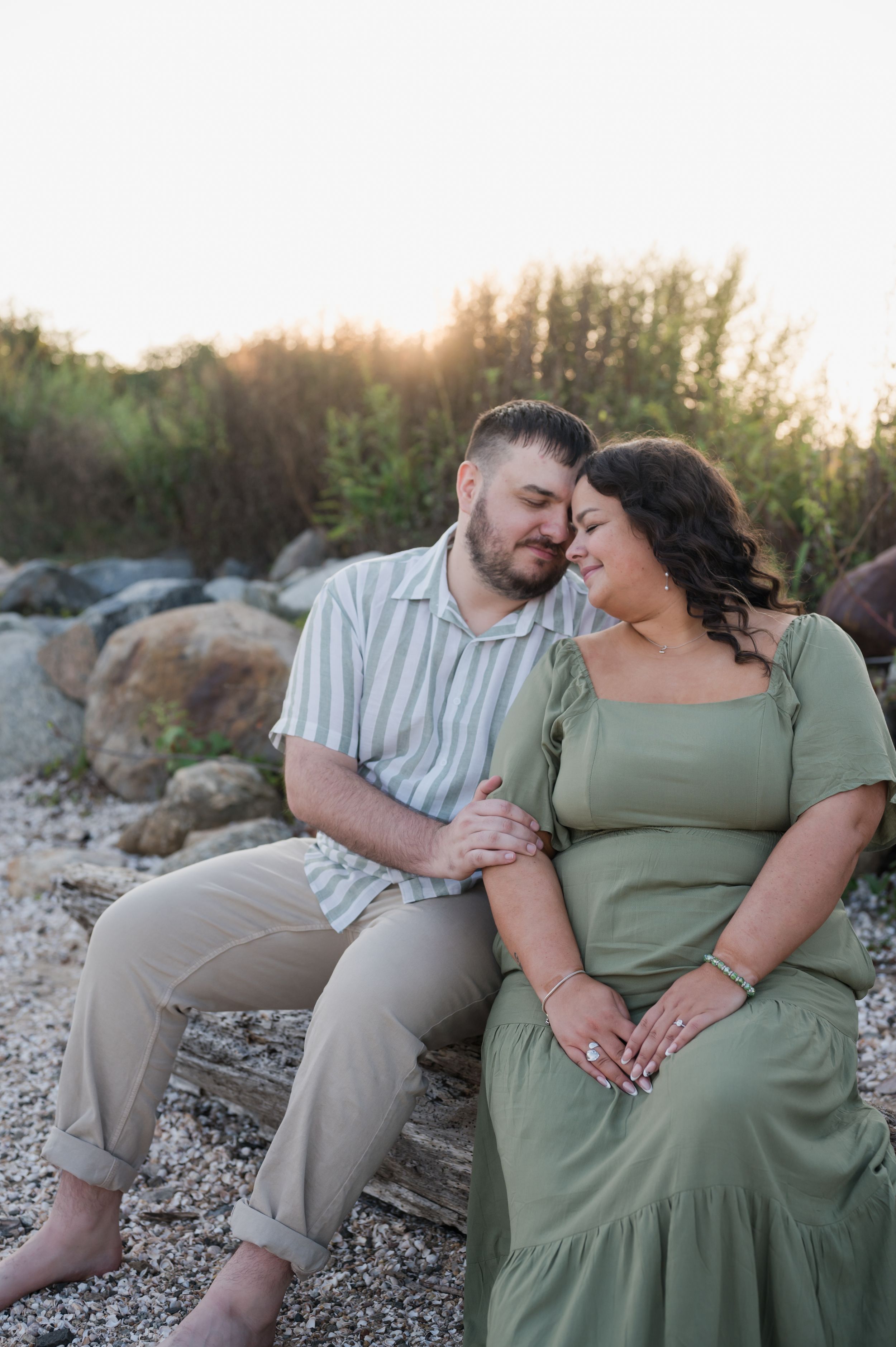 A couple shares an intimate moment while sitting on a rocky beach at sunset. Hammonasset Beach State Park