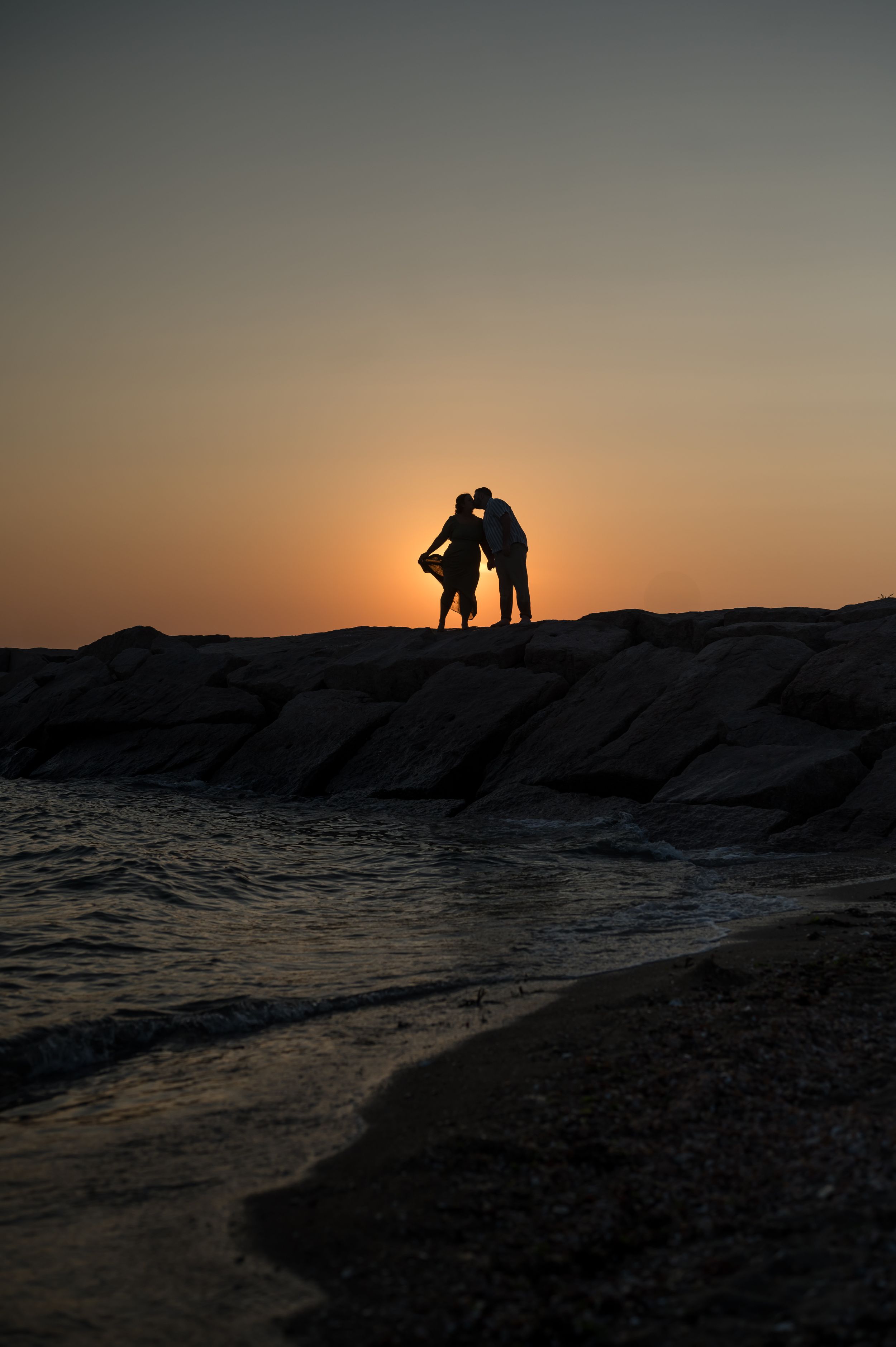Silhouettes of people stand against a dramatic sunset over the ocean. Hammonasset Beach State Park