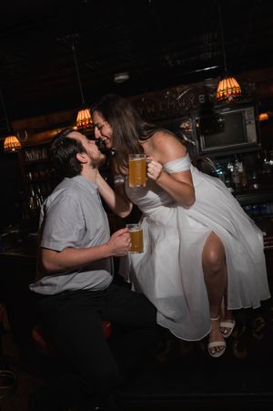 A playful moment captured at a bar between two people in white attire. Graduate Hotel by Hilton New Haven Old Heidelberg Bar