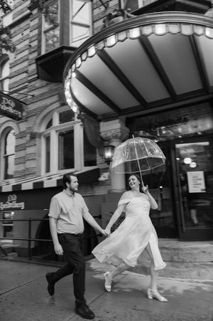 A couple runs playfully under an ornate theater marquee in black and white. Graduate Hotel by Hilton New Haven