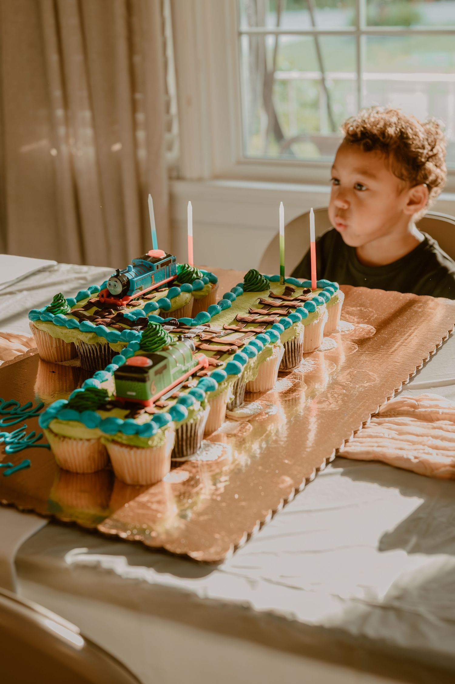 Cupcakes decorated in turquoise frosting and candles arranged in the shape of a train on a brown paper backdrop.
