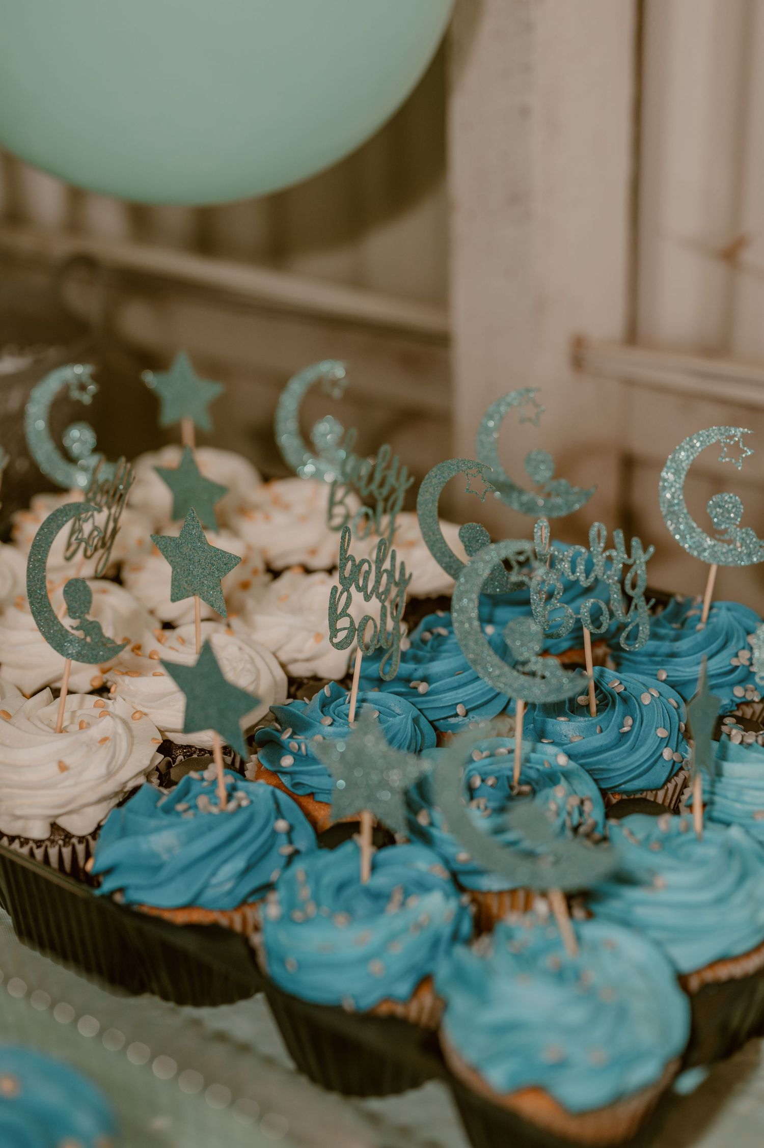Frosted cupcakes decorated with glittery blue and silver moon and star toppers arranged on a dessert tray. photo by Samantha Campbell imager