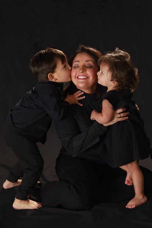 Mom being hugged & kisses by son and daughter on a dark background