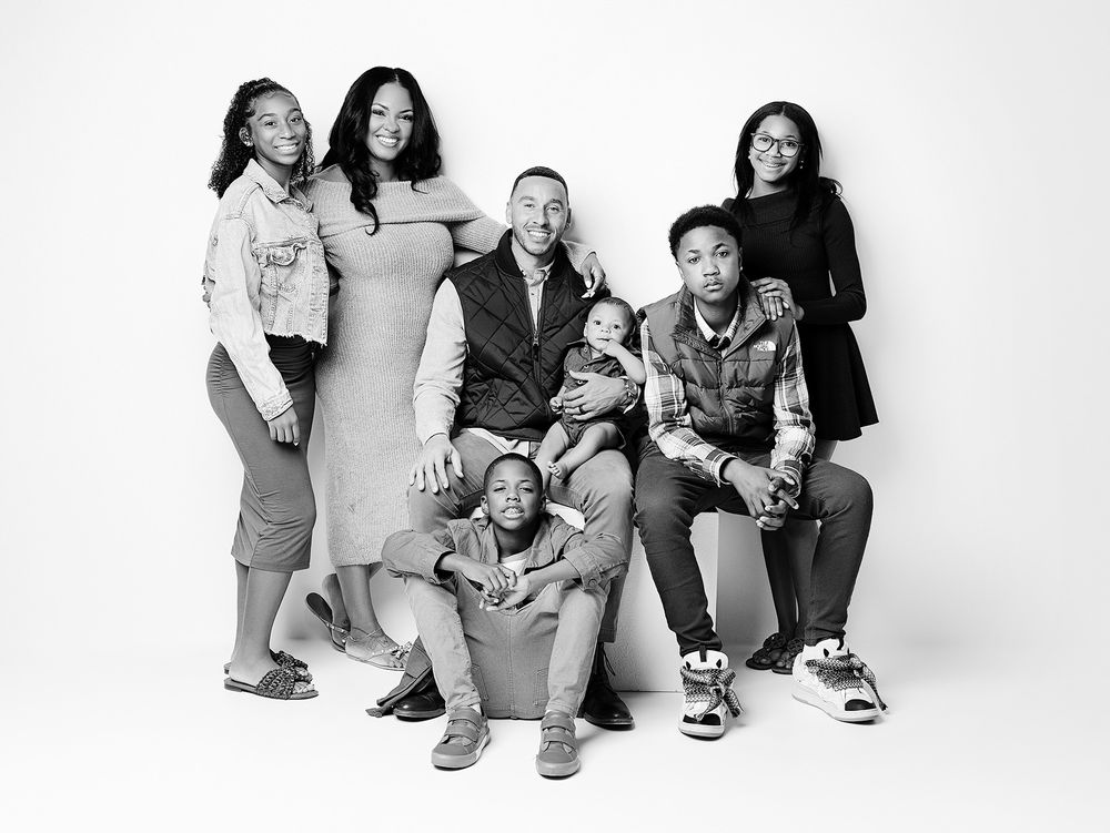 Black and white studio portrait of a family group of six people posing together against a white backdrop.