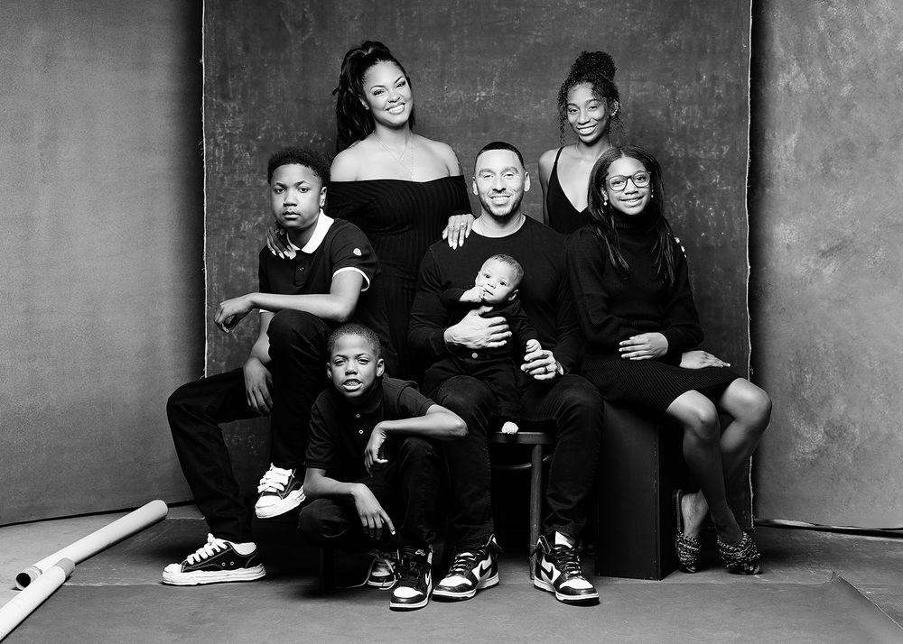 A black and white portrait of a group wearing matching black outfits sitting and posing together against a studio backdrop.