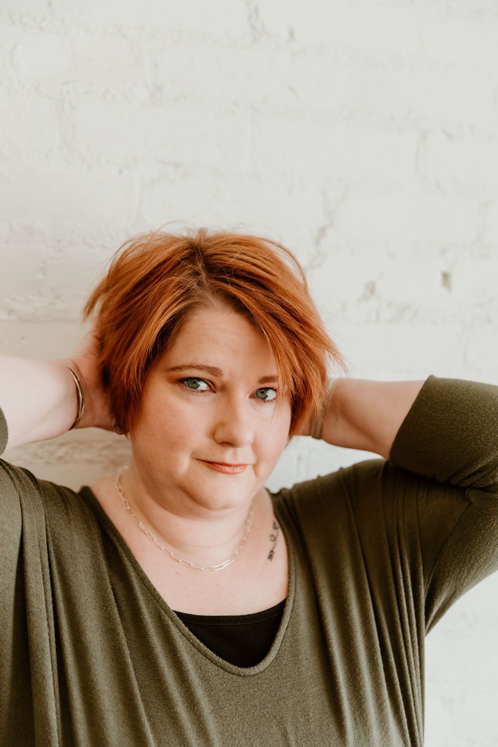 A person with red hair wearing an olive green shirt poses against a white wall in a series of expressive shots.