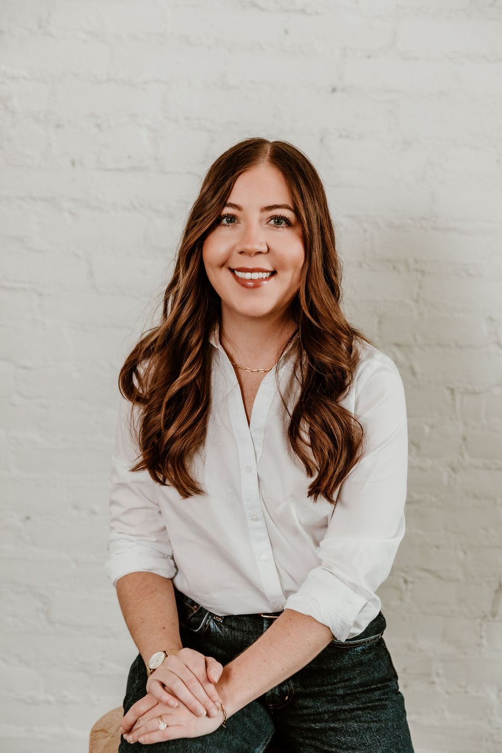 Professional studio portrait series against white brick wall showing casual business style in white shirt and dark pants.