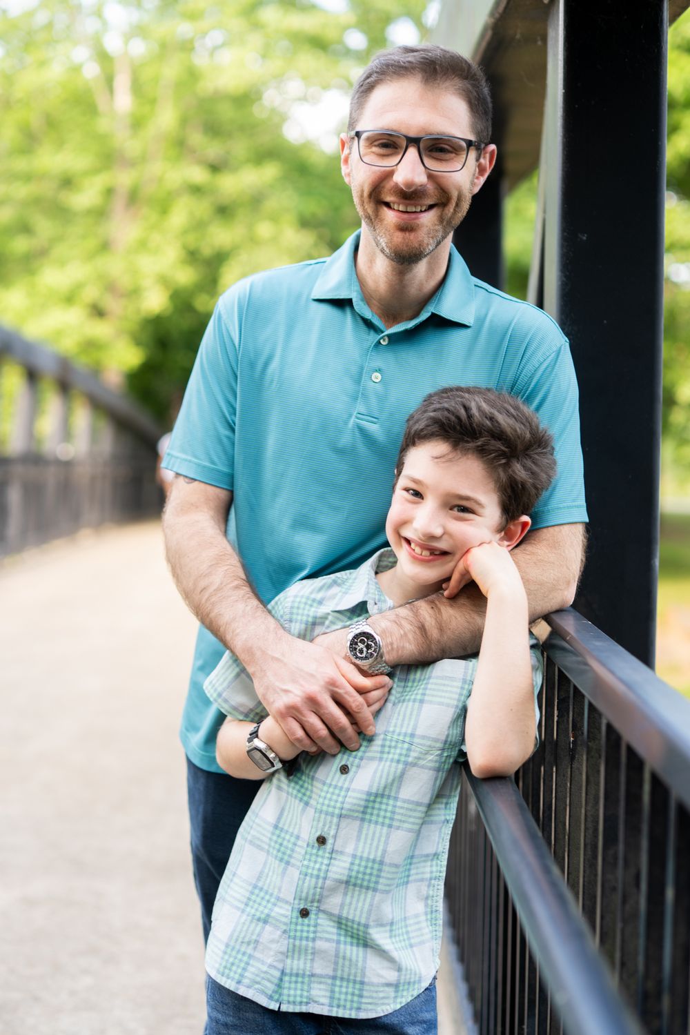 A father and son standing on a bridge smiling at the camera
