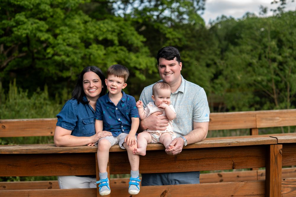 A family on a wooden bridge sitting on the edge smiling