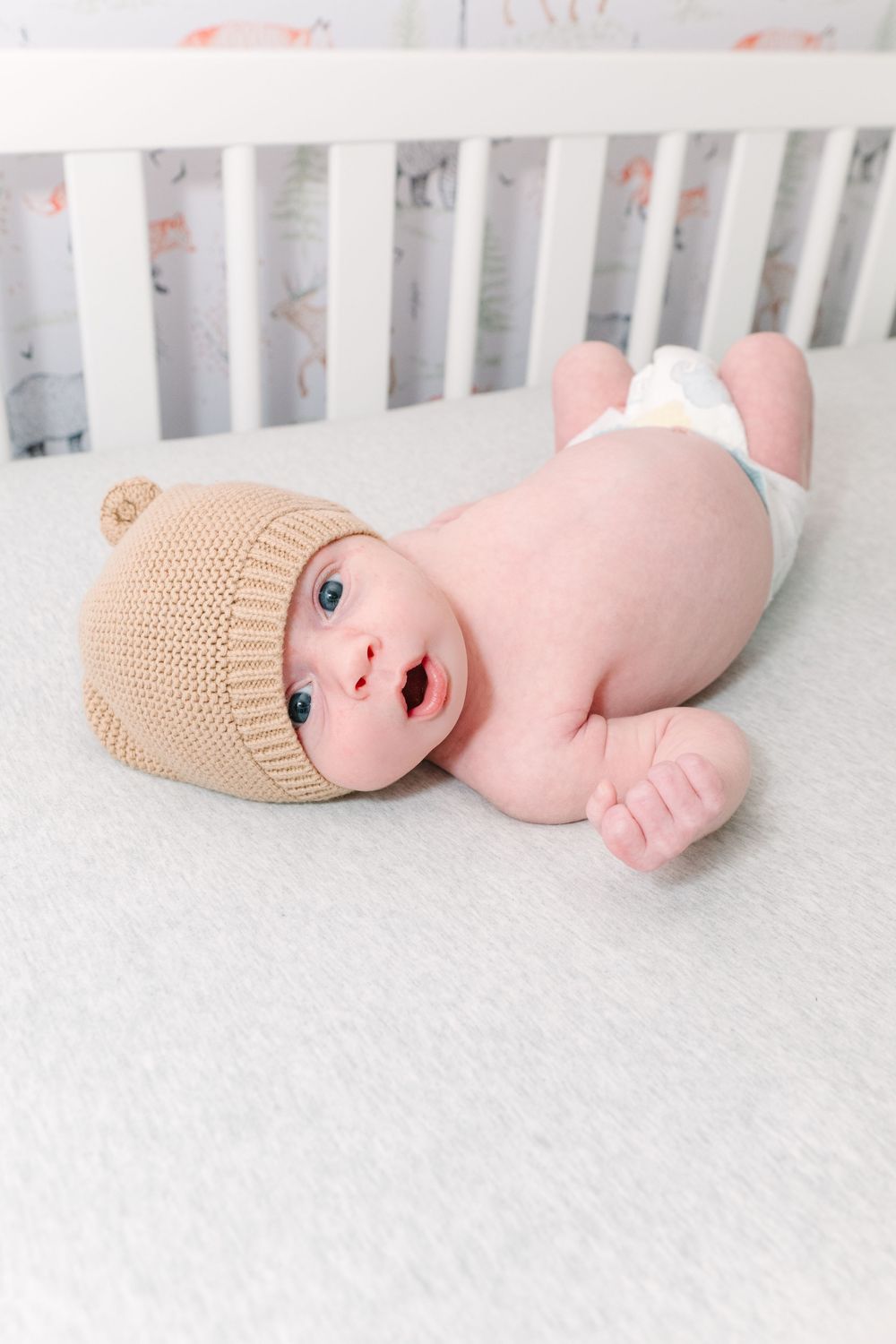Sleeping newborn baby in white lying on soft white bedding with outstretched arms.
