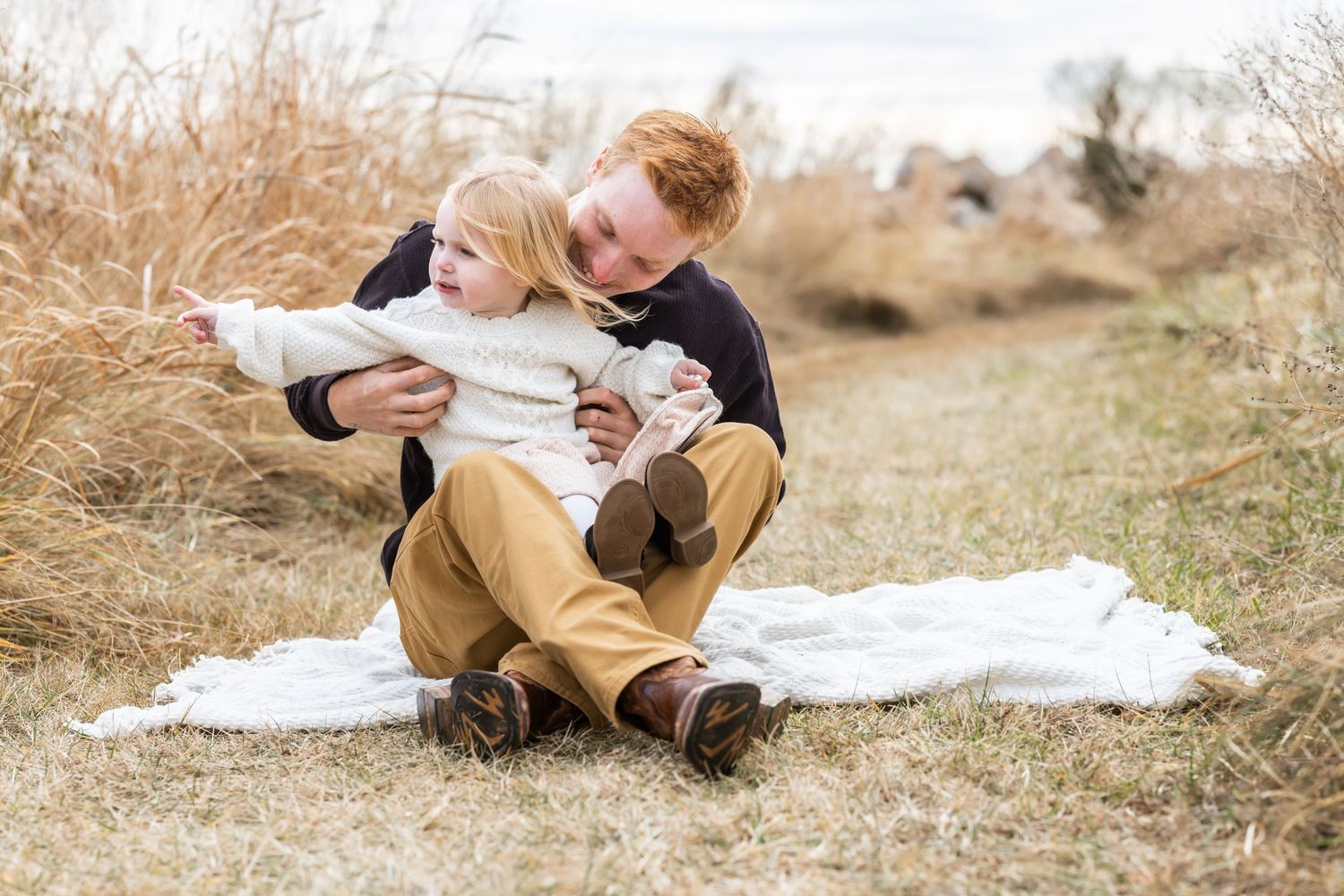 A father and daughter sit together on a blanket in a golden field during an intimate outdoor photo session.
