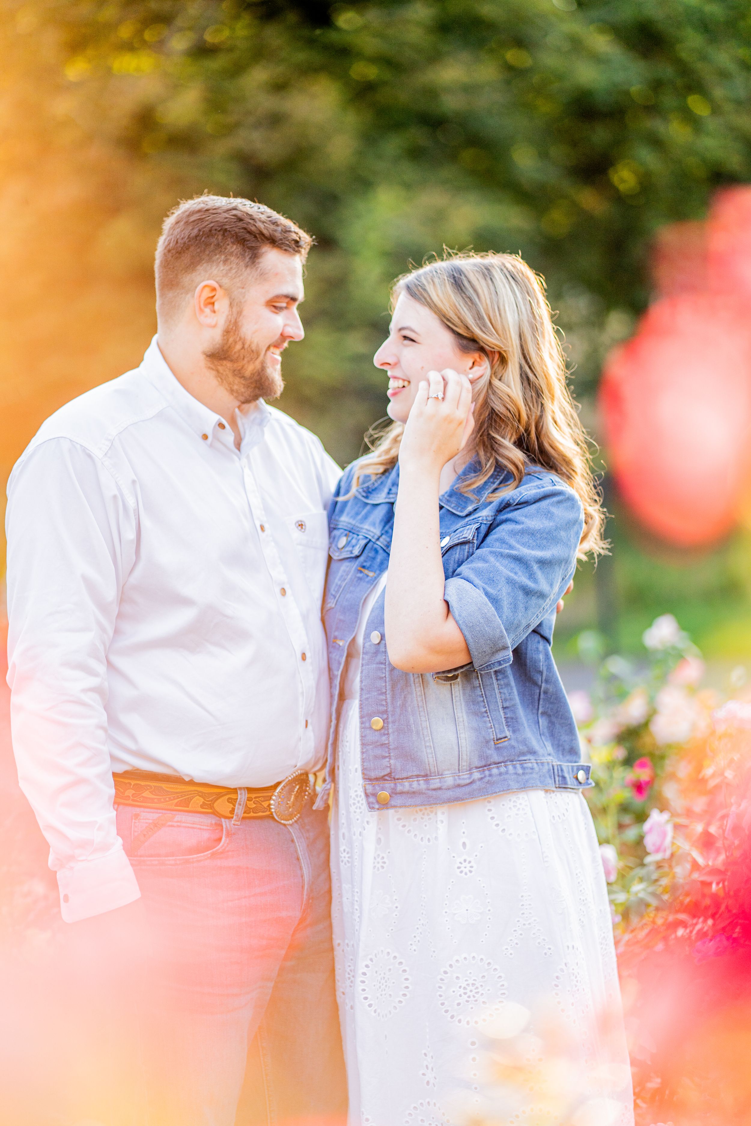 A romantic couple in a garden setting share tender moments among blooming flowers and soft sunlit bokeh effects.