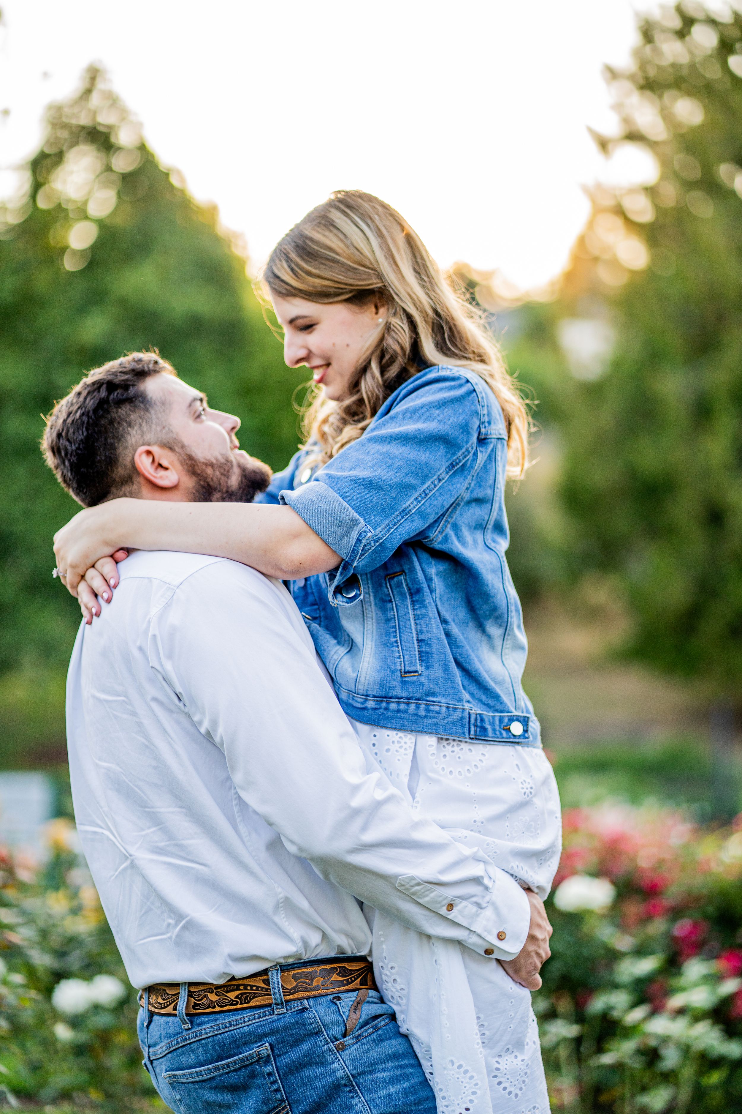 A couple embraces joyfully in a garden setting during sunset with roses in the background.
