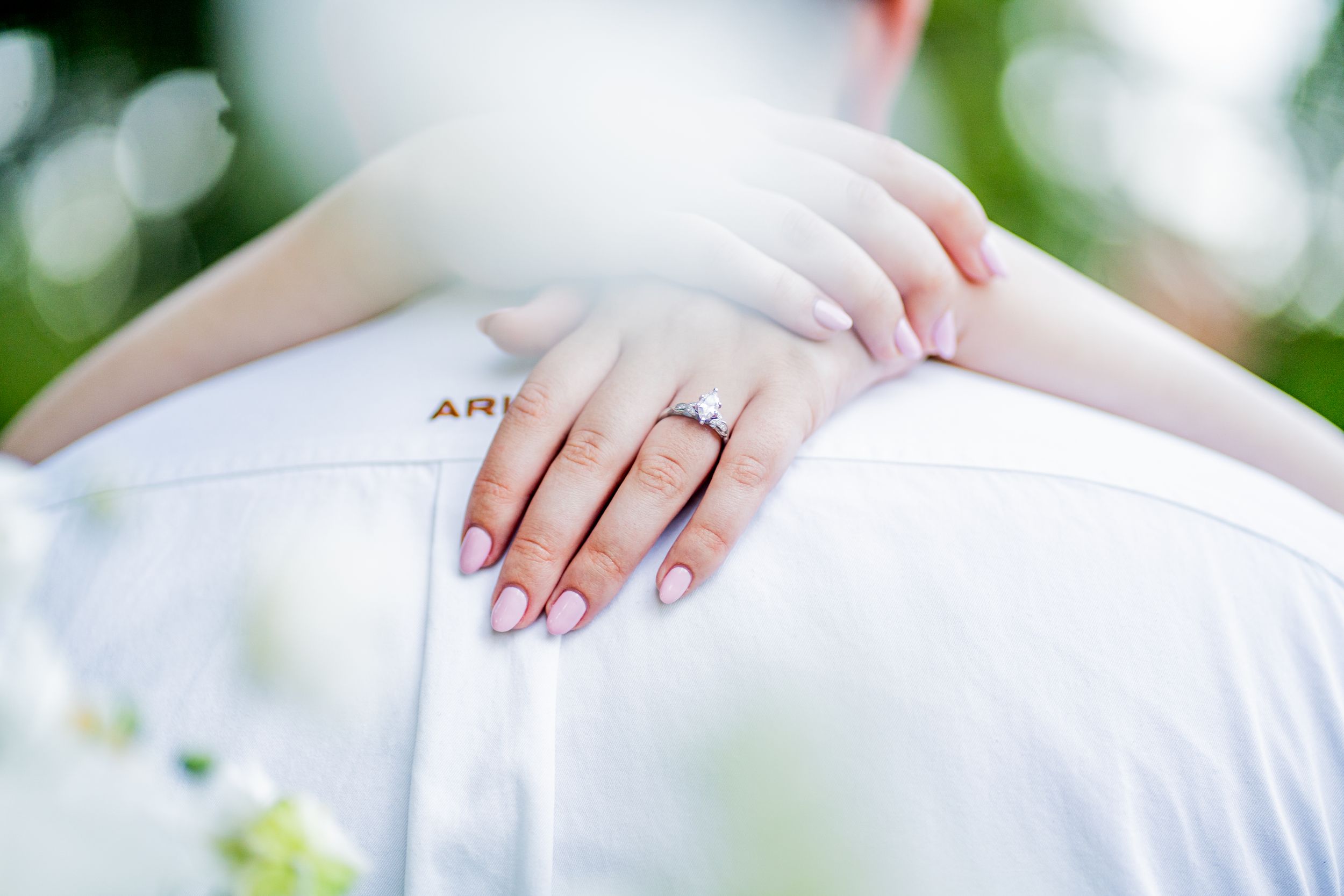 Close-up view of hands exchanging wedding rings during an outdoor ceremony with blurred greenery in background.