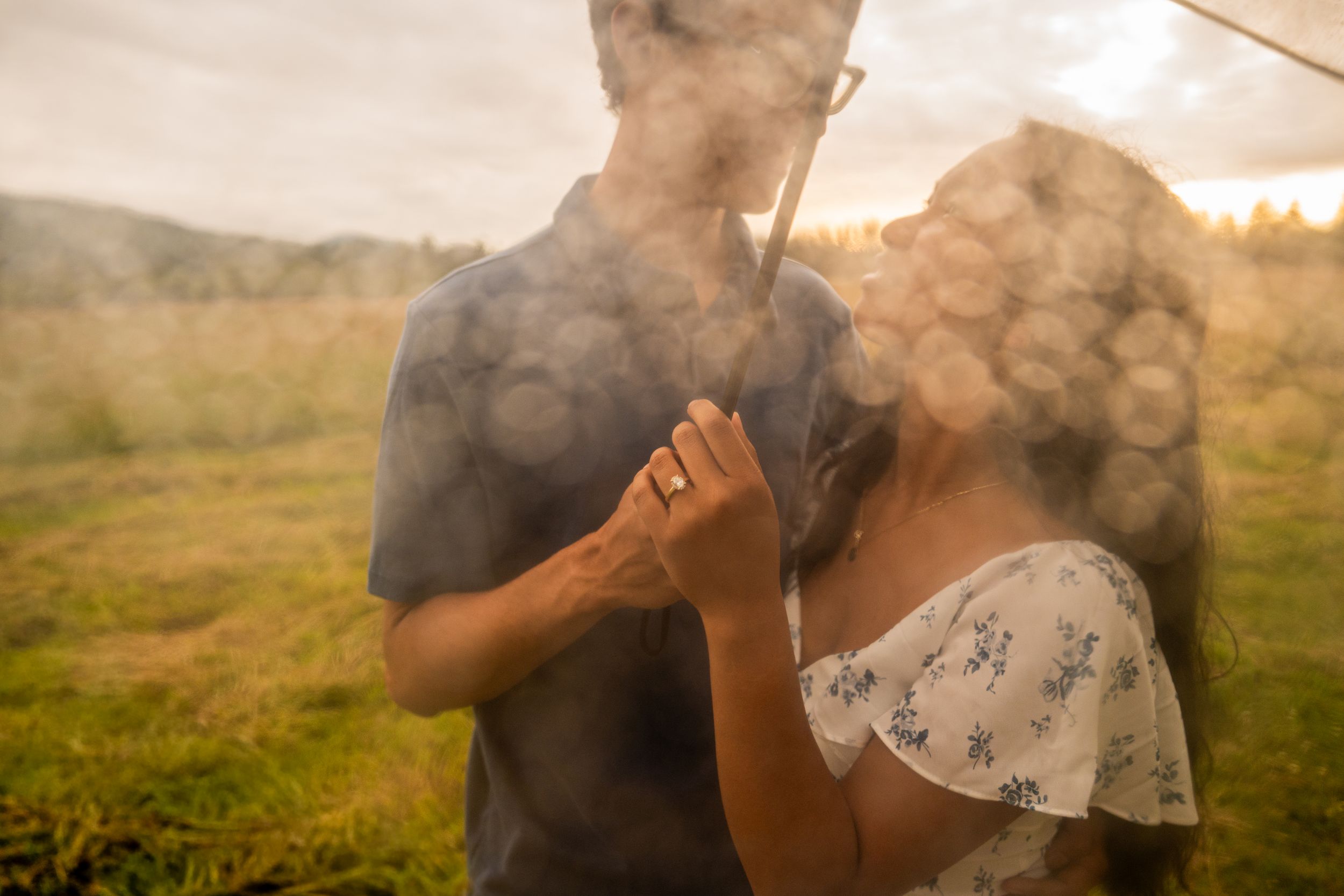 Couple sharing a romantic moment outdoors surrounded by smoke and golden light in a lush green field.