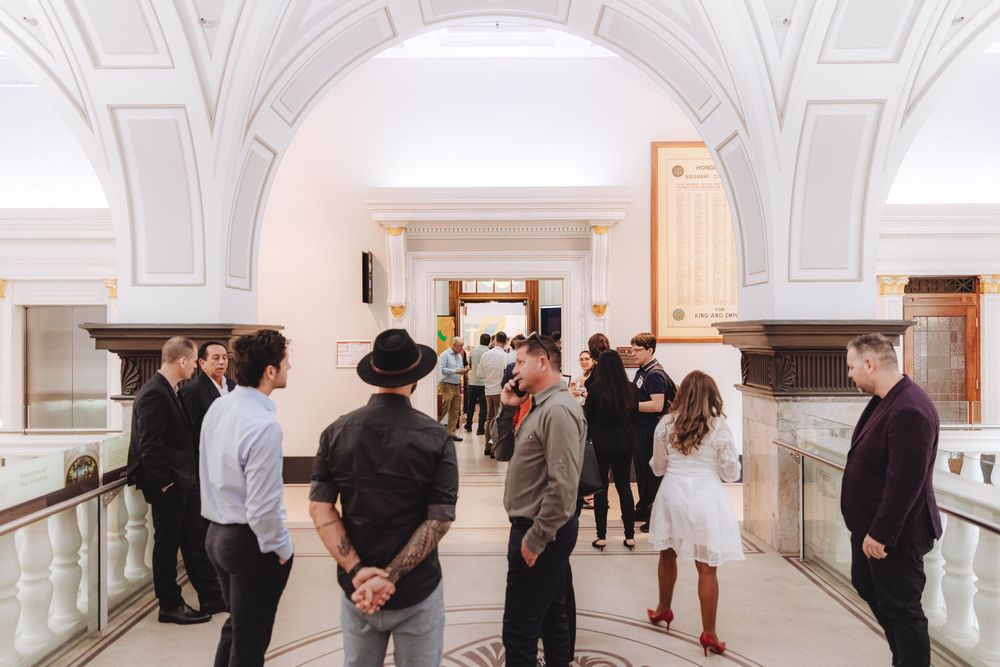 Visitors admire artwork in a bright white gallery hallway with ornate architectural details and crown molding.