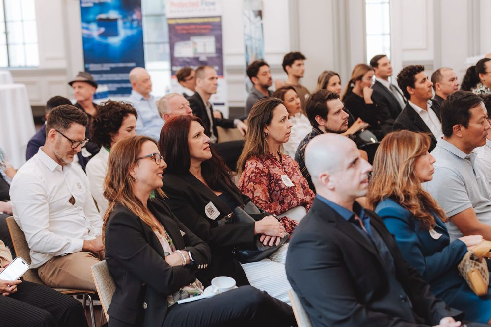 Business professionals listen attentively during a crowded conference presentation in a bright meeting room.