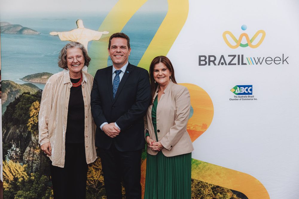 Business professionals gather at Brazil Week conference event with branded backdrop and coastal scenery display.