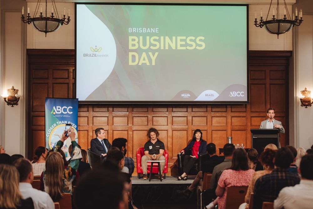Business conference attendees gather in an elegant wood-paneled room with chandeliers and presentation screens.