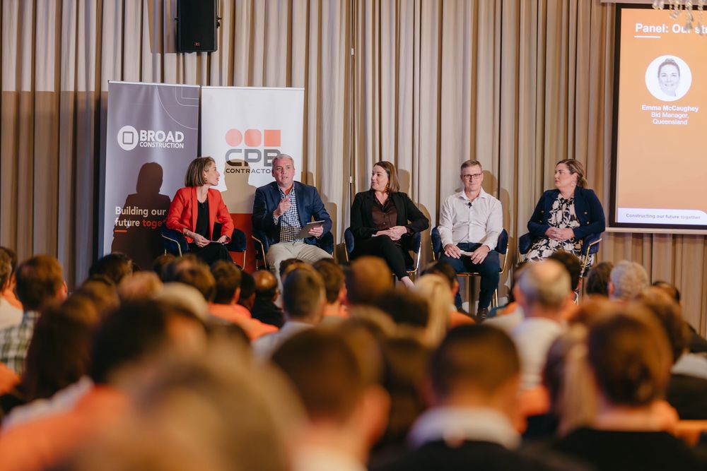 Business conference panel with speakers seated on stage addressing audience in formal setting.
