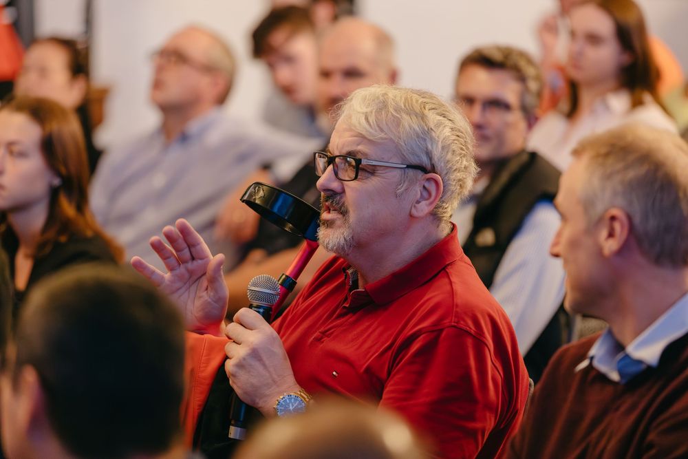 Person in a red sweater speaking into a microphone during a conference presentation.