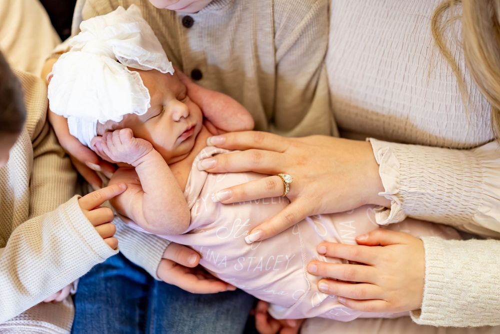 A person wearing a cream sweater holds and feeds a baby with a bottle while sitting on a couch.