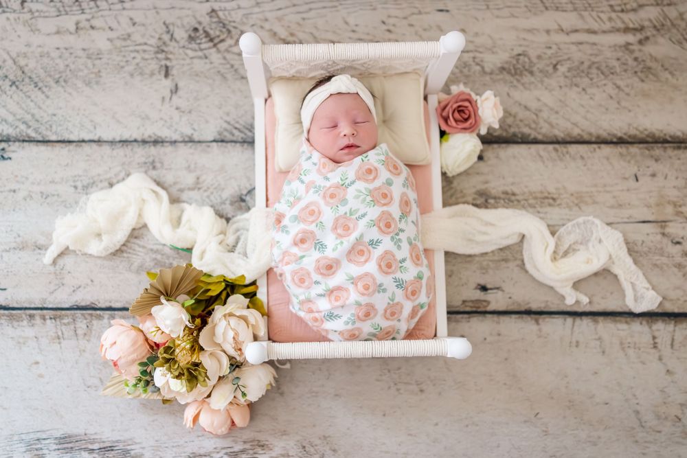 A rustic wooden backdrop with white decorative elements and soft pink floral accents creates a charming setting.