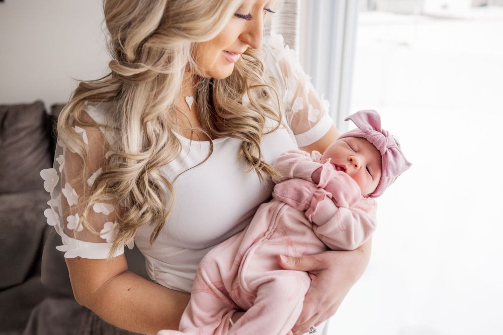 A tender moment between parent and newborn baby swaddled in pink blankets near a bright window.