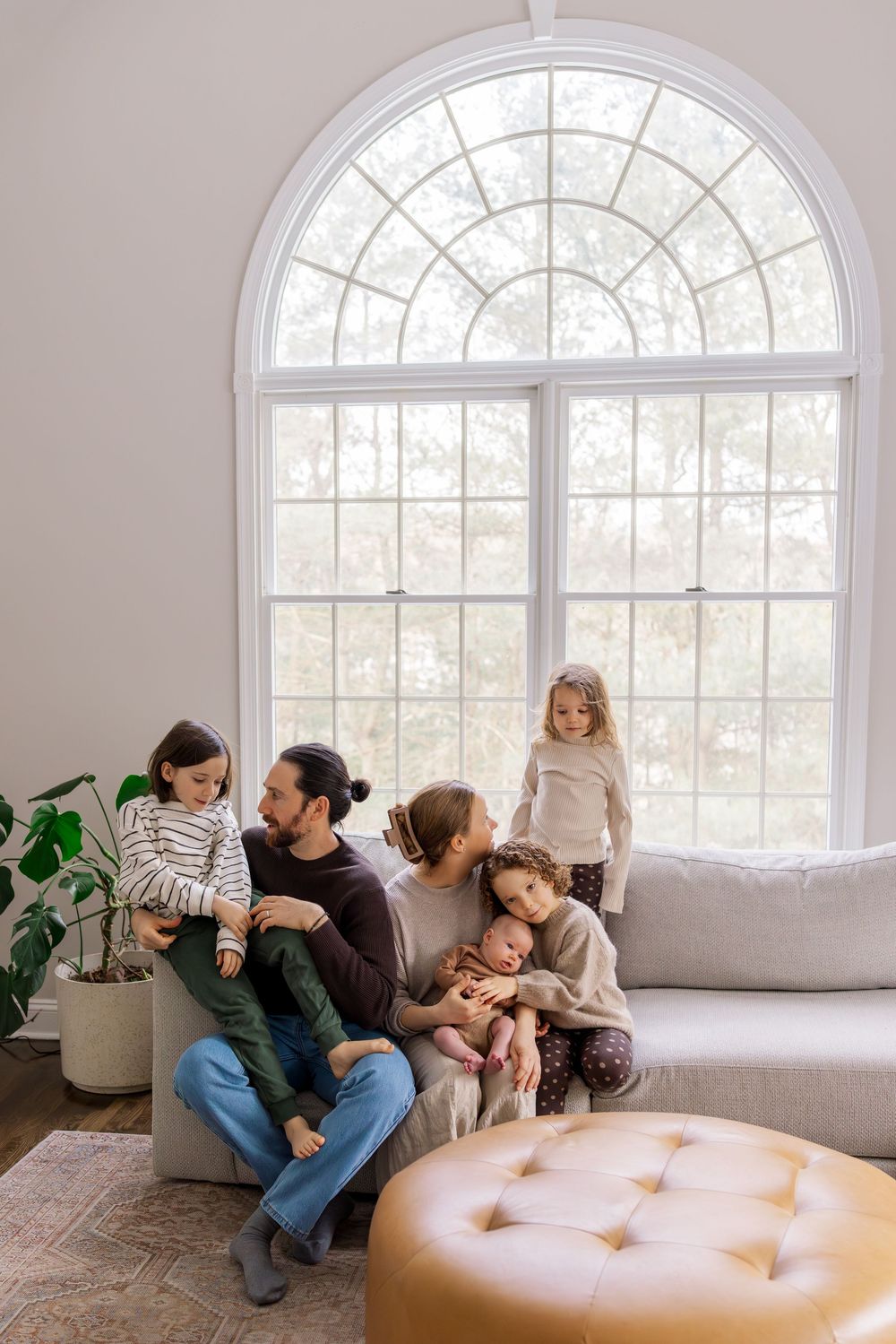 Family relaxing together on a white couch in a bright sunlit room with arched windows.