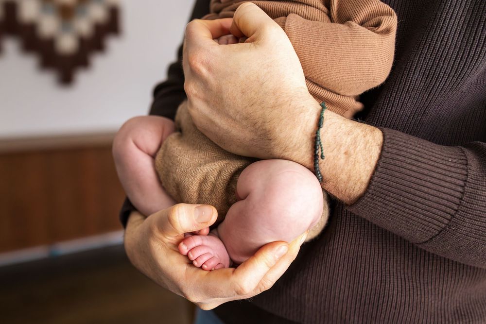 A person's hands hold and shape brown clay dough into a round form on a wooden surface.