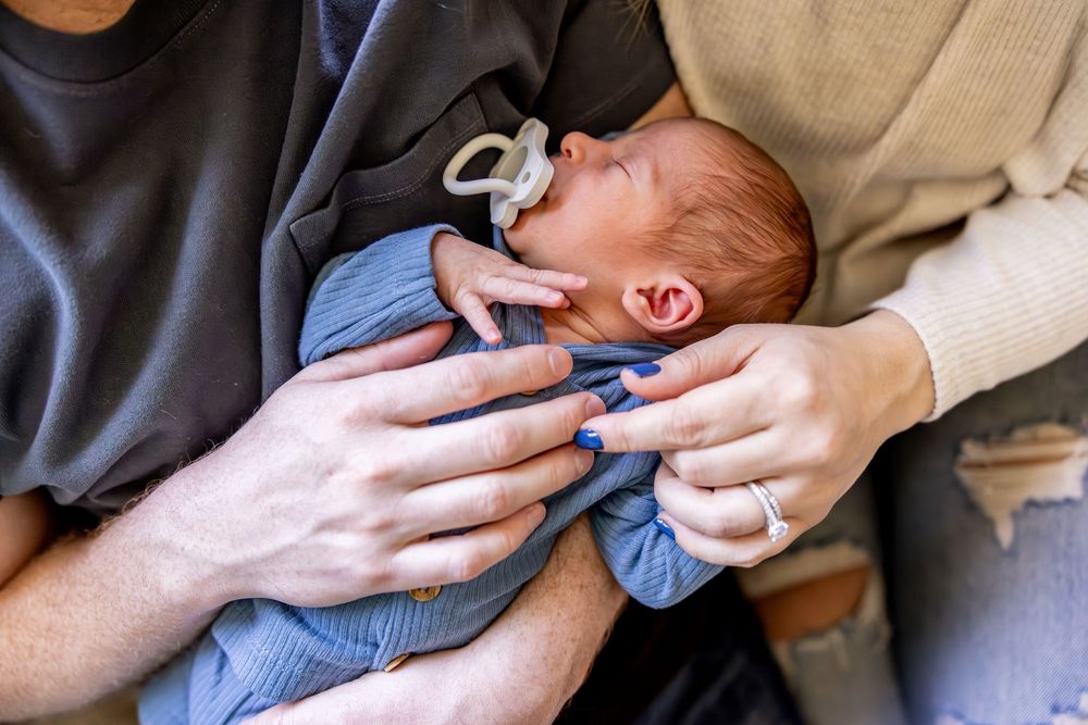 Baby in blue clothing being cradled in gentle hands while crying.