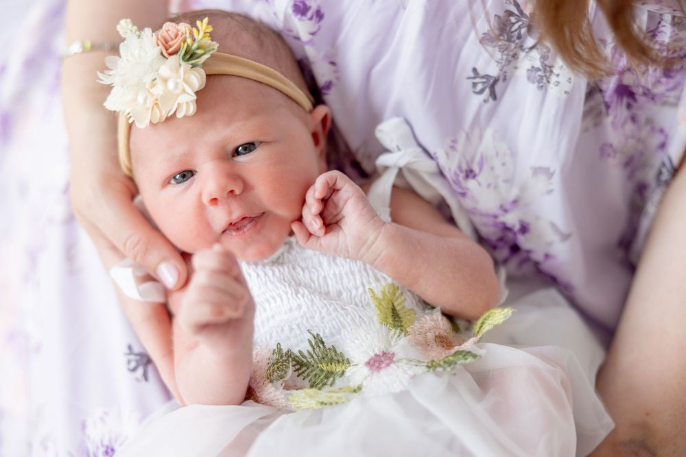 A baby lies on white bedding with floral accents and delicate decorative elements in a soft, dreamy setting.