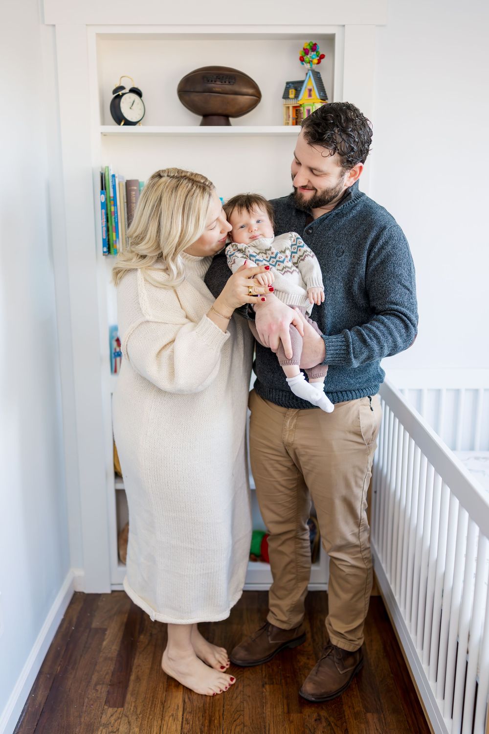Family shares tender moments with their newborn baby in a bright hallway with white walls and hardwood floors.