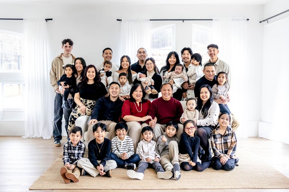 Large Asian family portrait with adults and children posing together in a bright white room for a formal group photo.