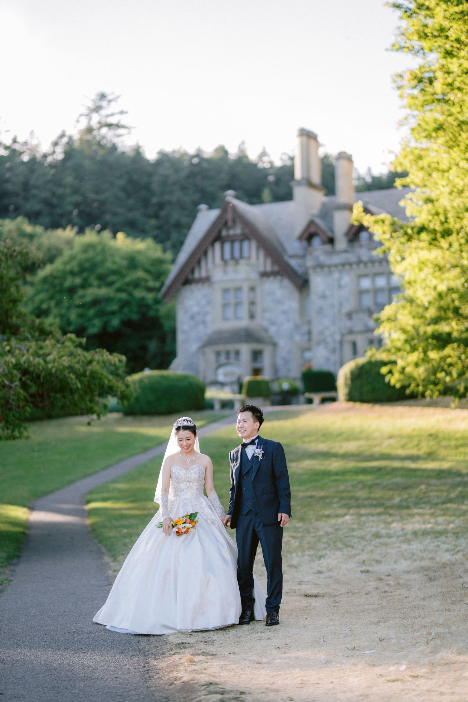 Wedding couple poses on path in front of charming Tudor-style mansion.