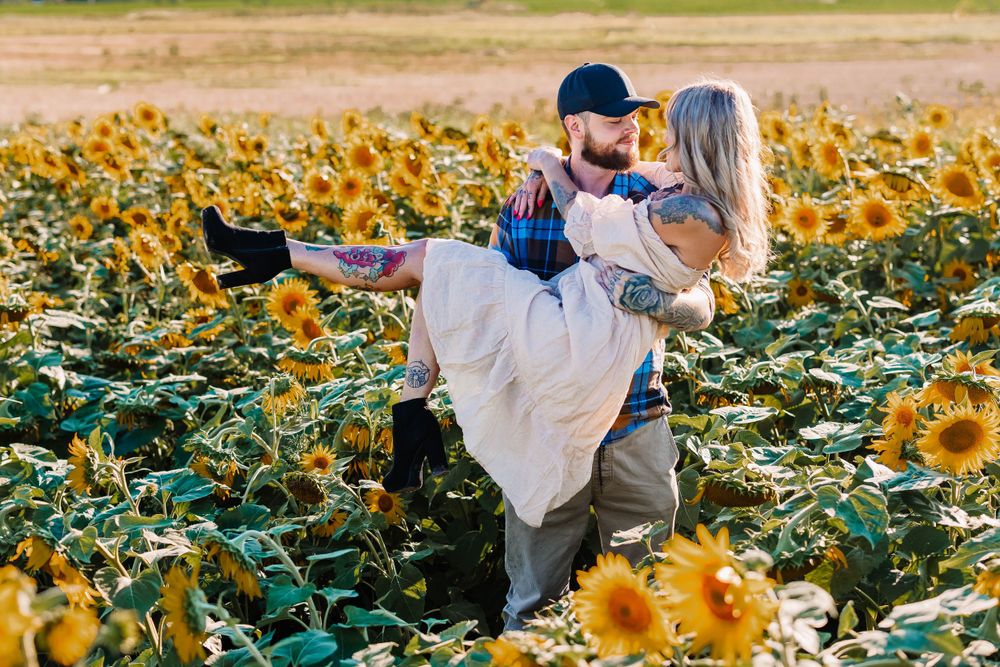 A romantic couple pose in a sunflower field during sunset.