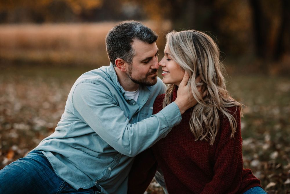 A romantic autumn photoshoot showing a couple sharing an intimate moment while sitting in fallen leaves.