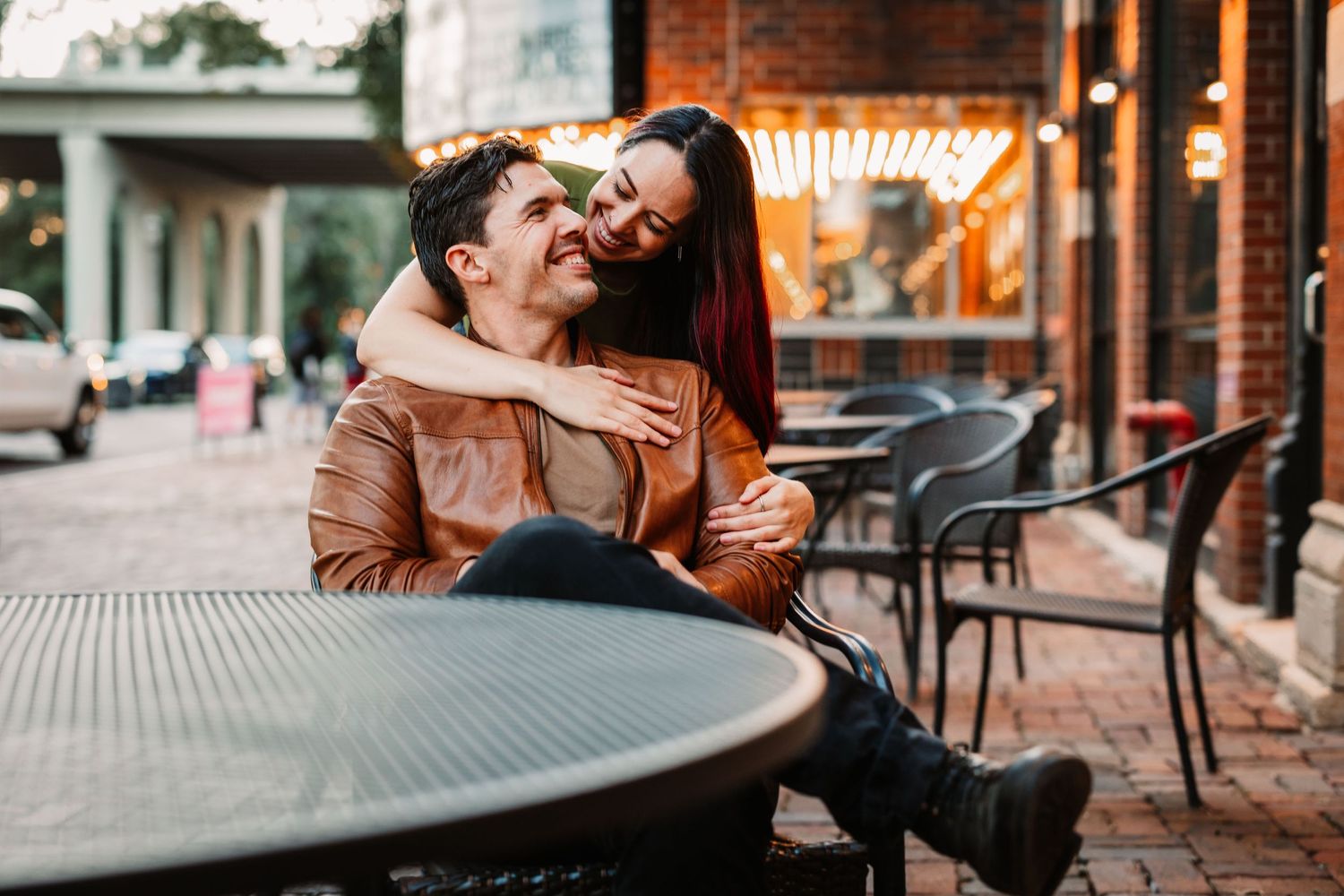 A tender embrace between two people near urban brick buildings and outdoor seating.