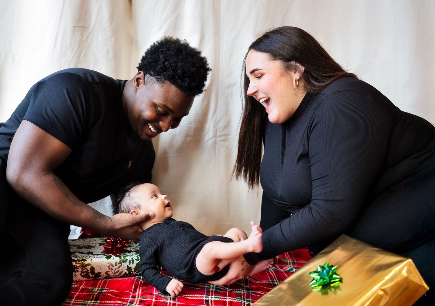 Family plays with baby on plaid blanket during holiday season.
