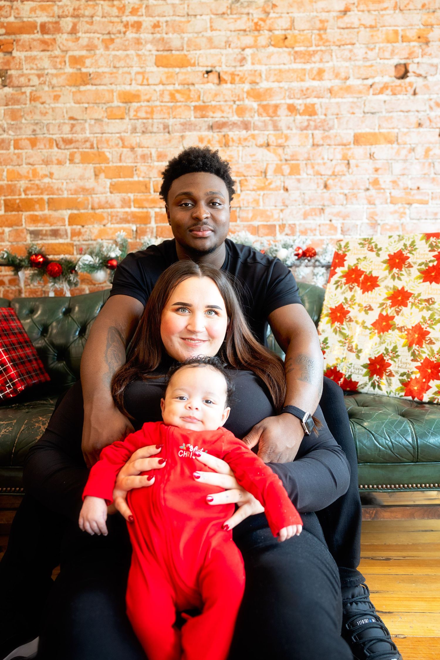 Family of three poses on vintage green couch with festive holiday decorations.