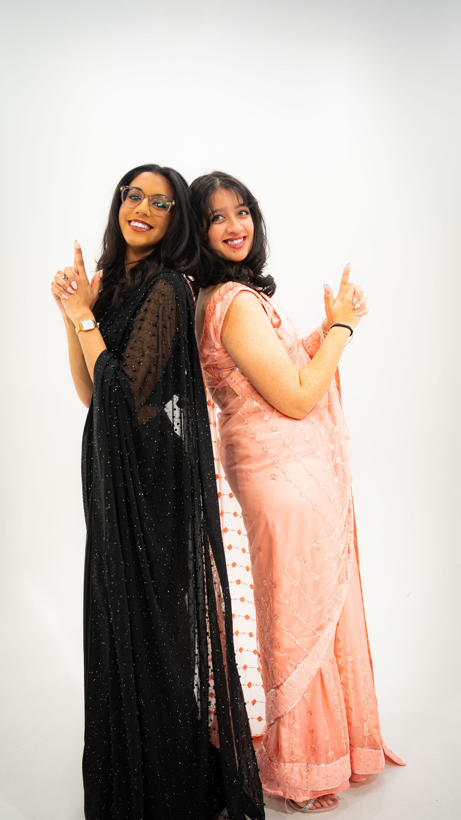 Two women in evening gowns, one black and one pink, posing back-to-back with peace signs.