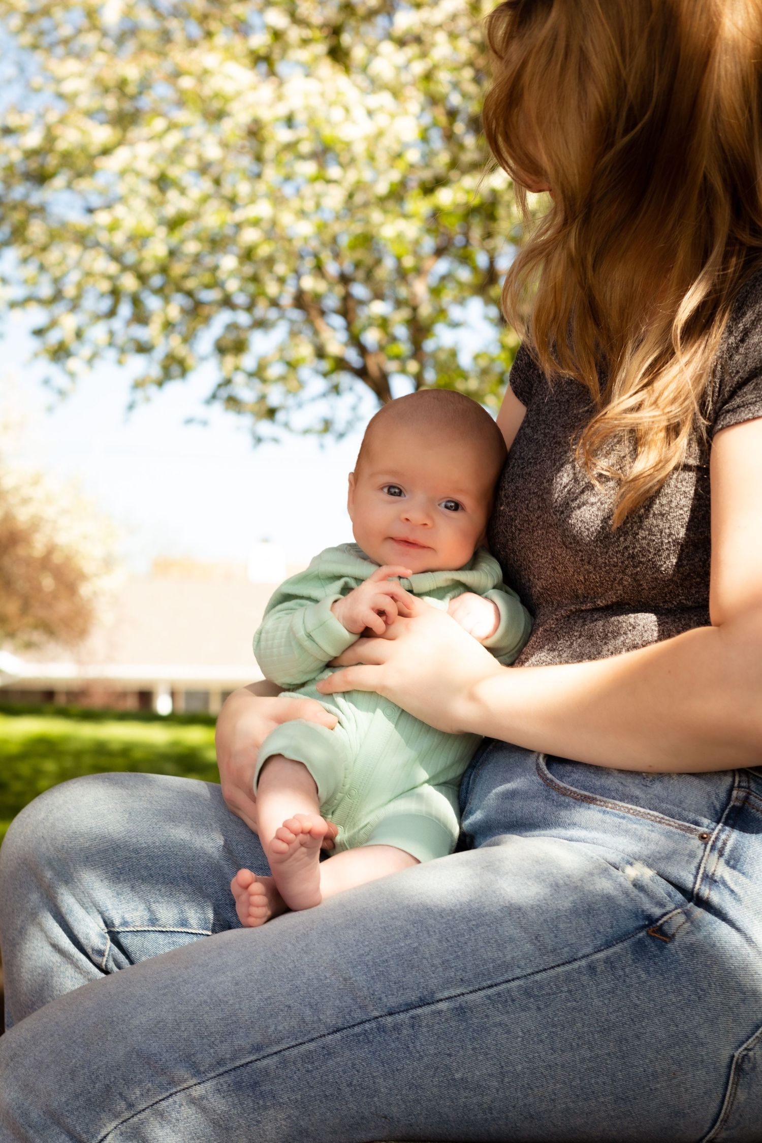 Baby in mint green outfit sitting on parent's lap outdoors in sunny garden setting.