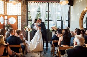 A bride and groom share their first kiss as husband and wife in a sunlit room surrounded by friends and family in Brooklyn New York