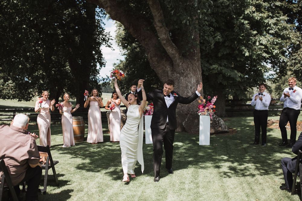 Wedding celebration in a shaded garden setting with guests gathered under trees.