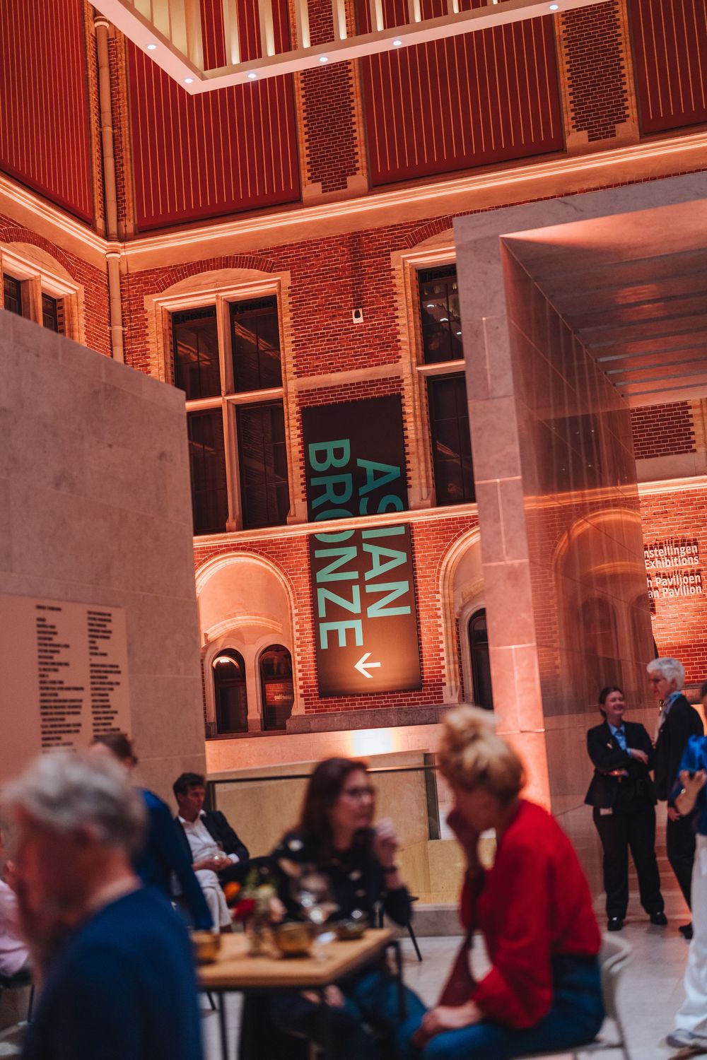 Interior view of modern exhibition space with architectural displays and visitors in brick-walled gallery with accent lighting.