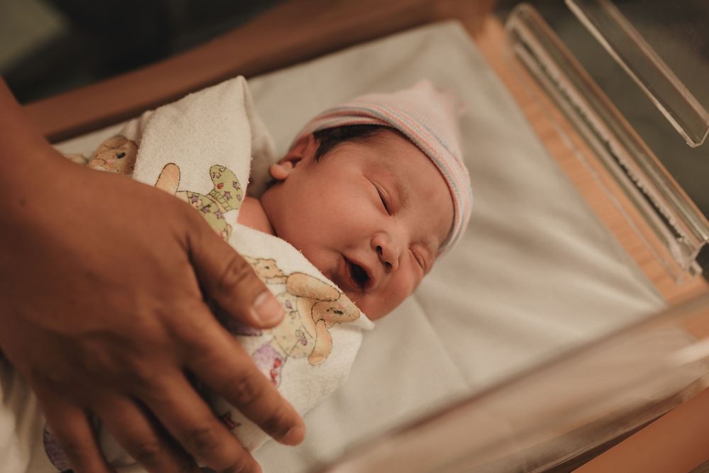 A newborn baby sleeps peacefully while swaddled in white blankets.
